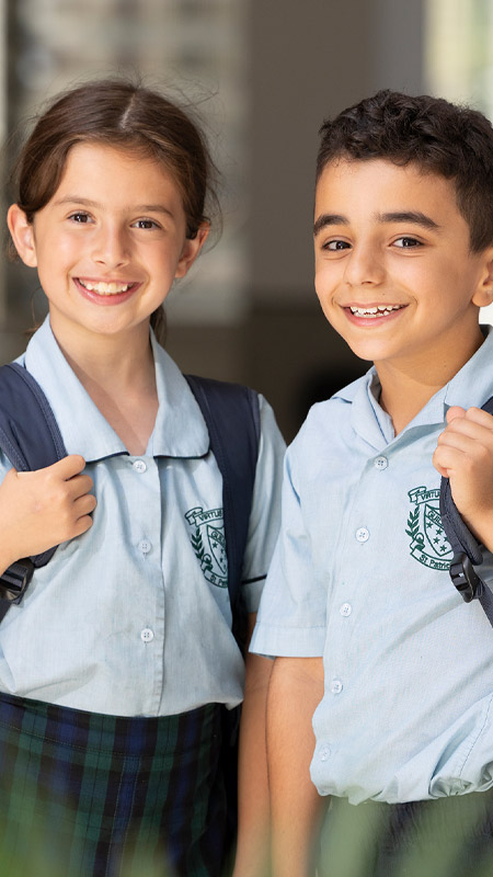 Two happy students from St Patrick's Primary School Guildford. The students are standing in the classroom and are wearing their backpacks.